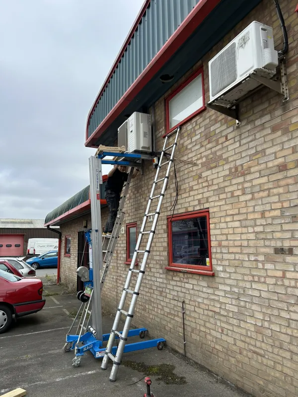 Engineer lifting an outdoor air conditioning unit into place with a material lift