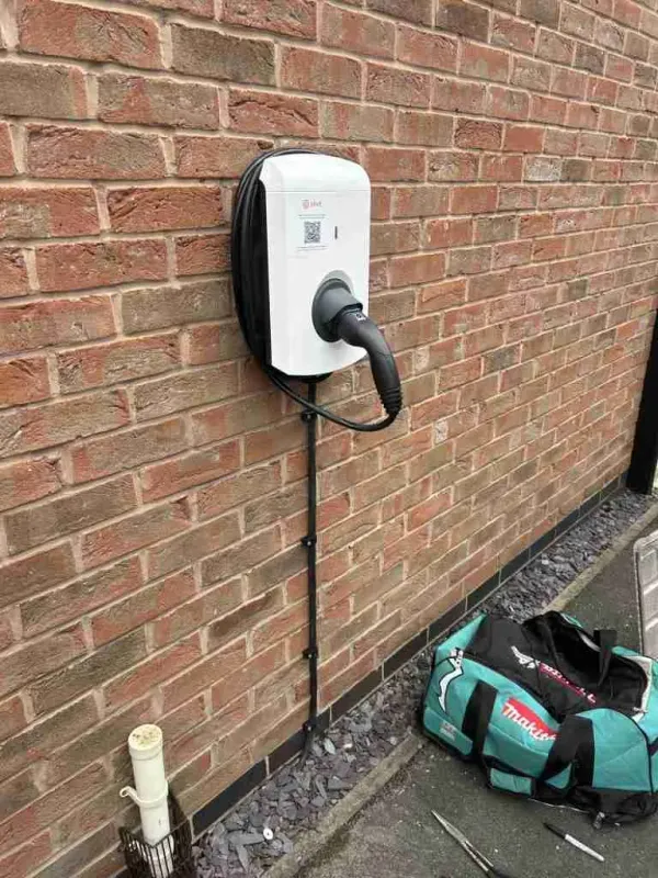 White wall-mounted EV charger with tethered cable on a brick wall
