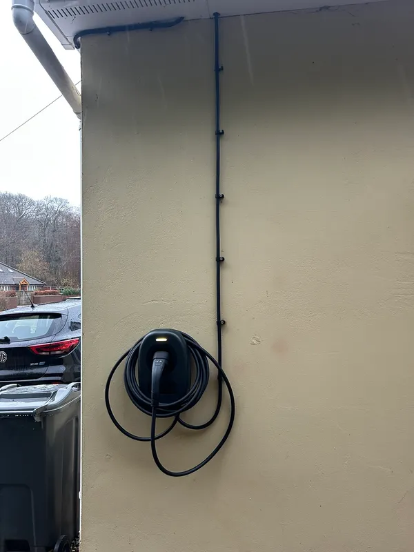 Black EV charger with tidy conduit run on a rendered house wall beside an electric car