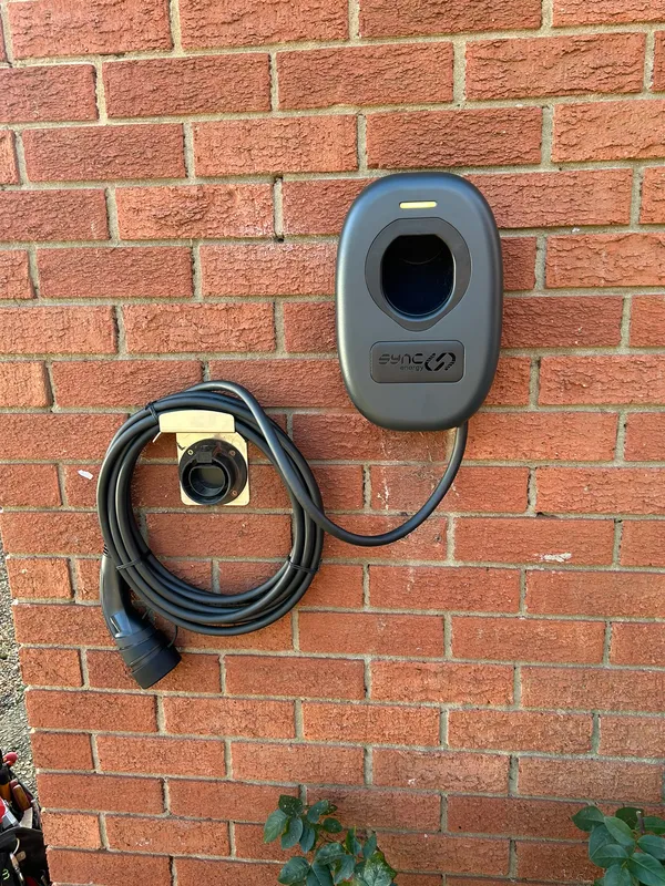 Sync Energy EV charger and holster mounted on a red brick wall